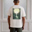 Person wearing a  paradaiza white t-shirt with a graphic design on the back, standing against a light-colored wall.