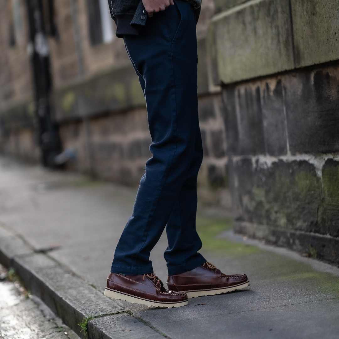Person wearing paradaiza  dark blue pants and brown shoes on a sidewalk.
