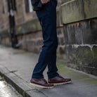 Person wearing paradaiza  dark blue pants and brown shoes on a sidewalk.