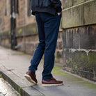 Person wearing paradaiza  dark blue pants and brown shoes on a sidewalk.