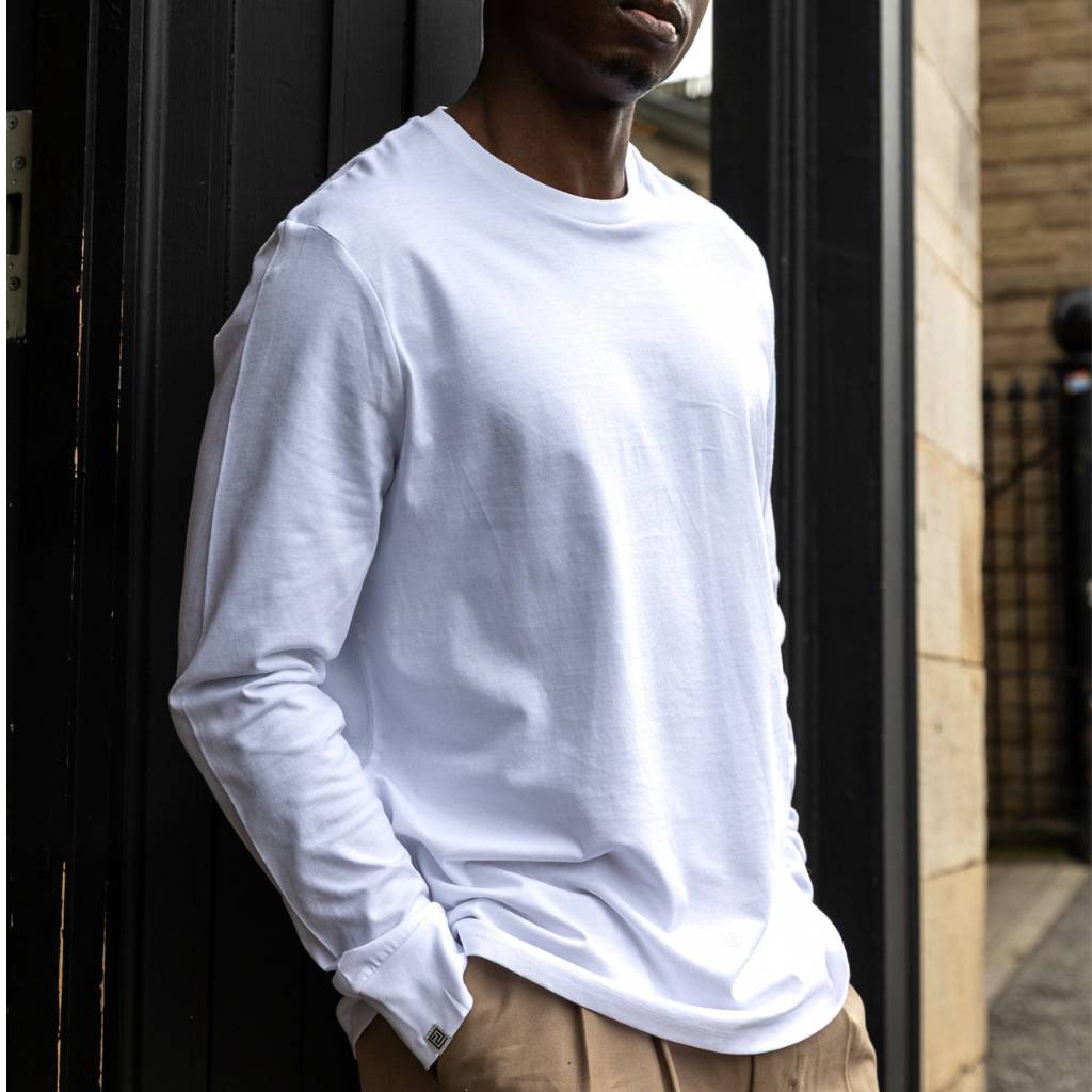 Person wearing a paradaiza white long-sleeve shirt and beige pants standing against a dark door.