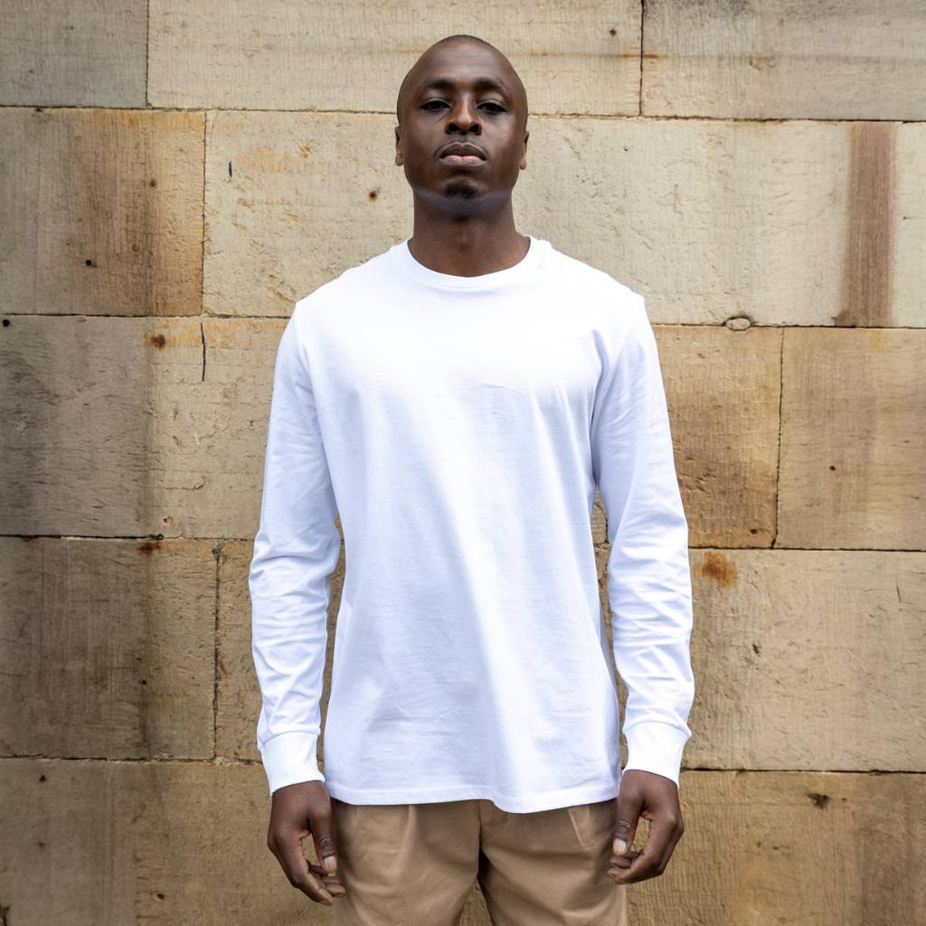 Man wearing a paradaiza white long-sleeve shirt standing against a wooden wall.