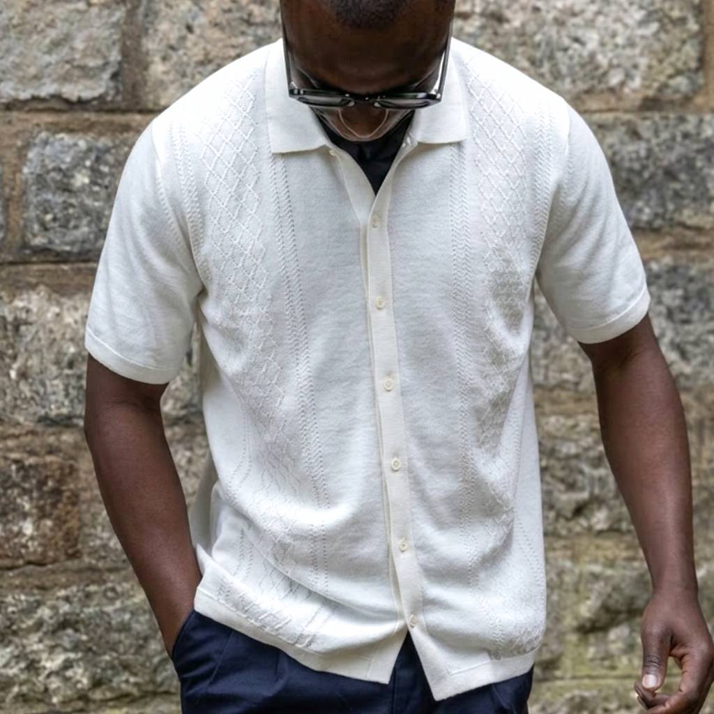 Man wearing a paradaiza white textured shirt and dark pants against a stone wall.