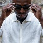 paradaiza white textured shirt and dark pants against a stone wall.