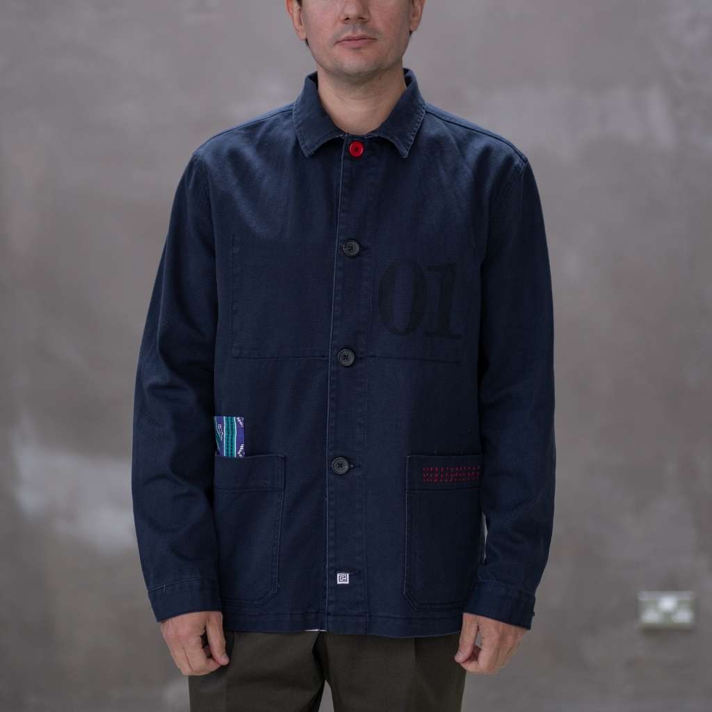Model wearing a  paradaiza dark blue worker jacket with patterned accents and sashiko stitching  in a studio.