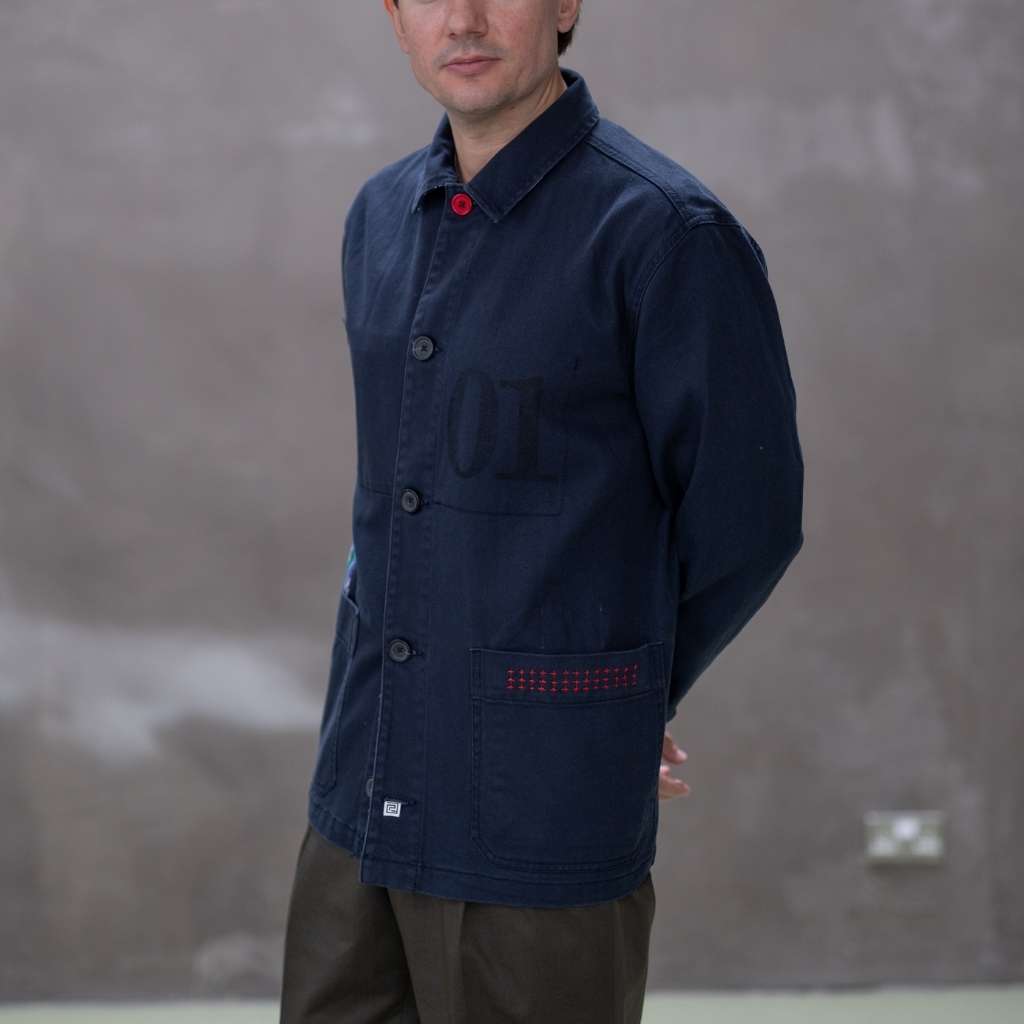 Model wearing a  paradaiza dark blue worker jacket with patterned accents and sashiko stitching  in a studio.