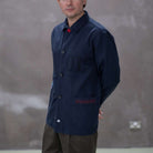 Model wearing a  paradaiza dark blue worker jacket with patterned accents and sashiko stitching  in a studio.
