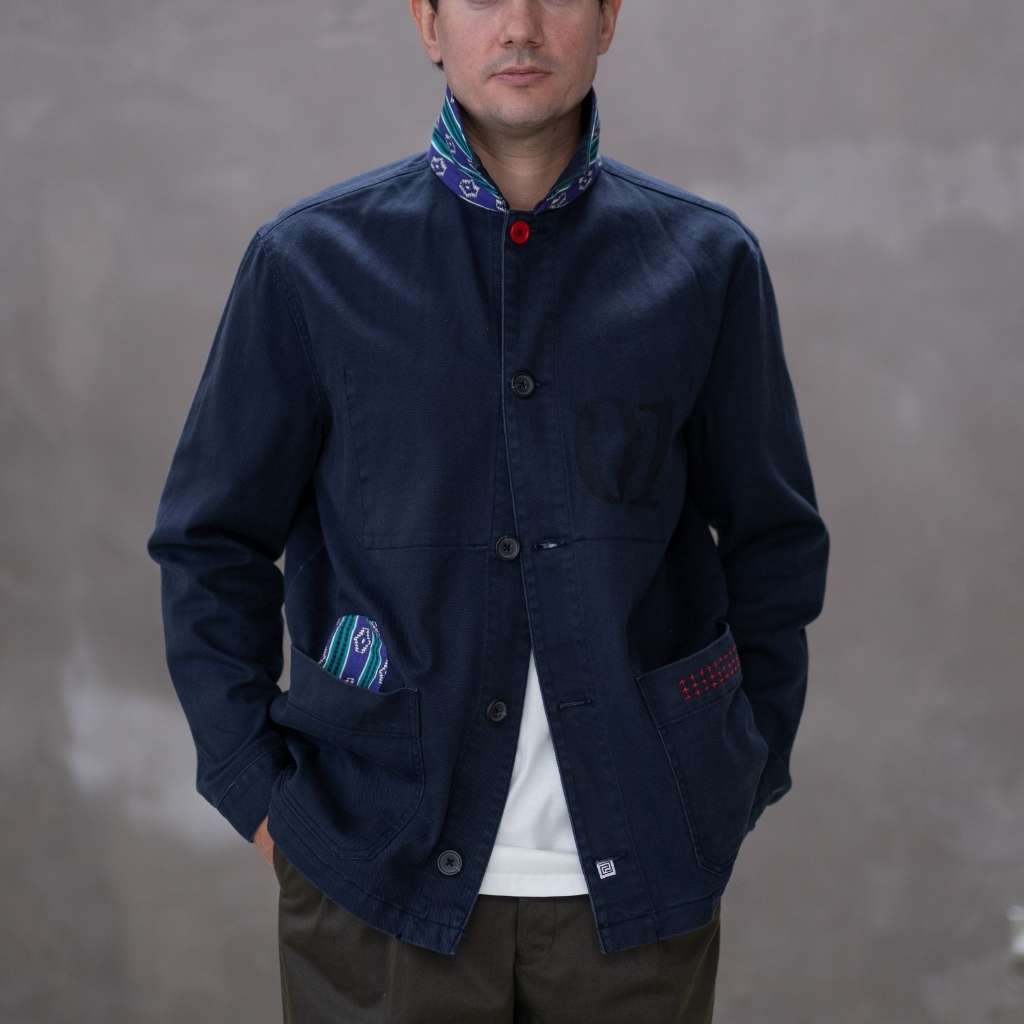 Model wearing a  paradaiza dark blue worker jacket with patterned accents and sashiko stitching  in a studio.