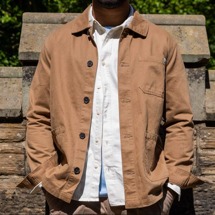 Man wearing a tan paradaiza worker  jacket over a white shirt with a blurred green background