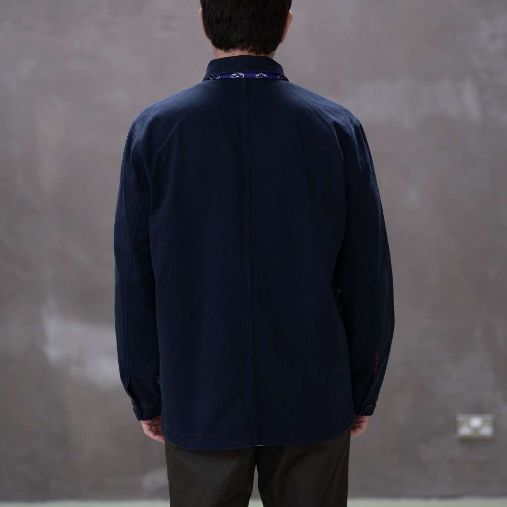 Model wearing a  paradaiza dark blue worker jacket with patterned accents and sashiko stitching  in a studio.