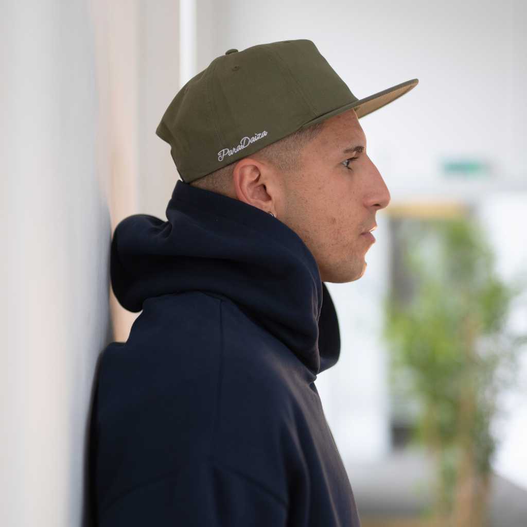 Man wearing a  paradaiza khaki cap and dark hoodie against a neutral background