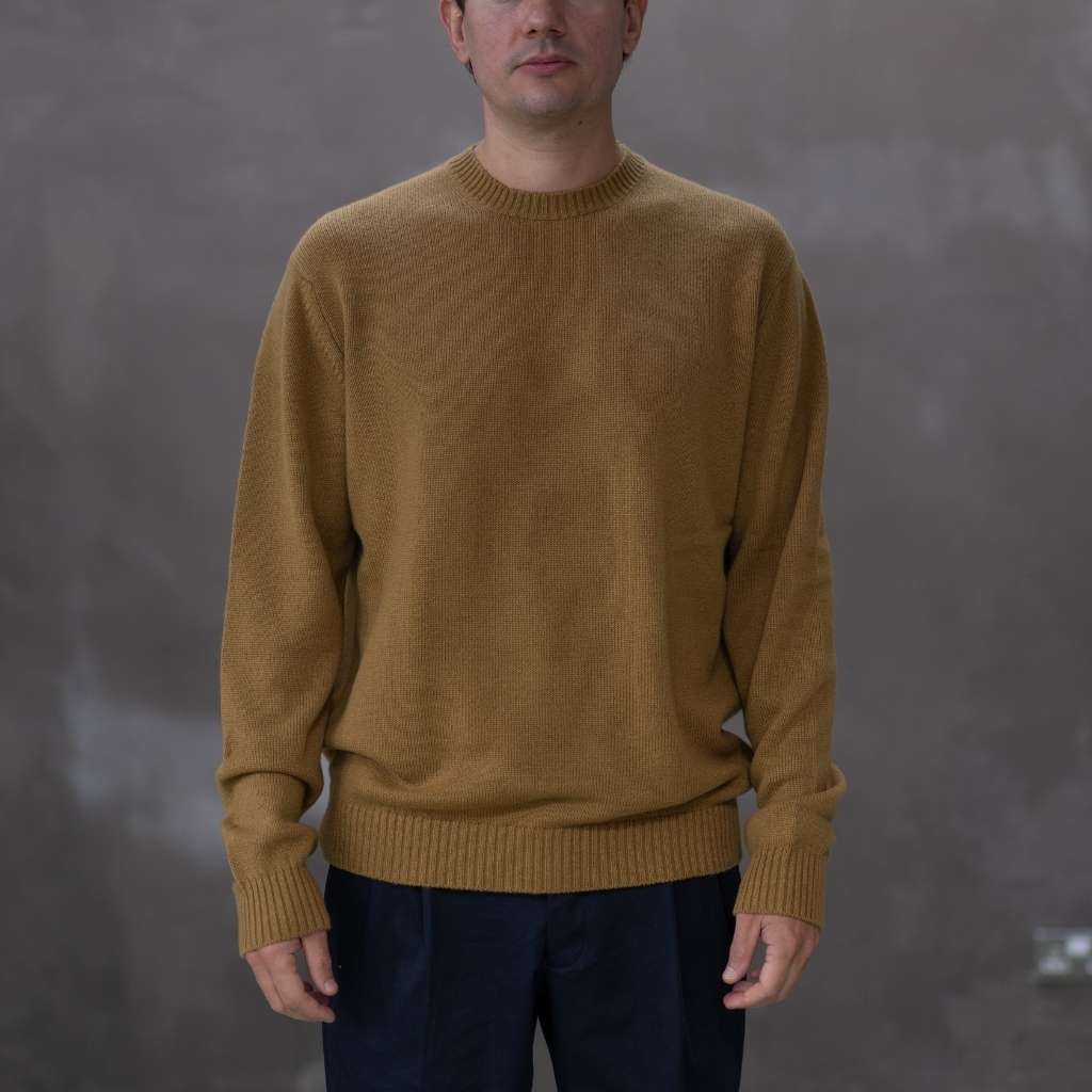 Man wearing a paradaiza mustard yellow sweater against a grey background