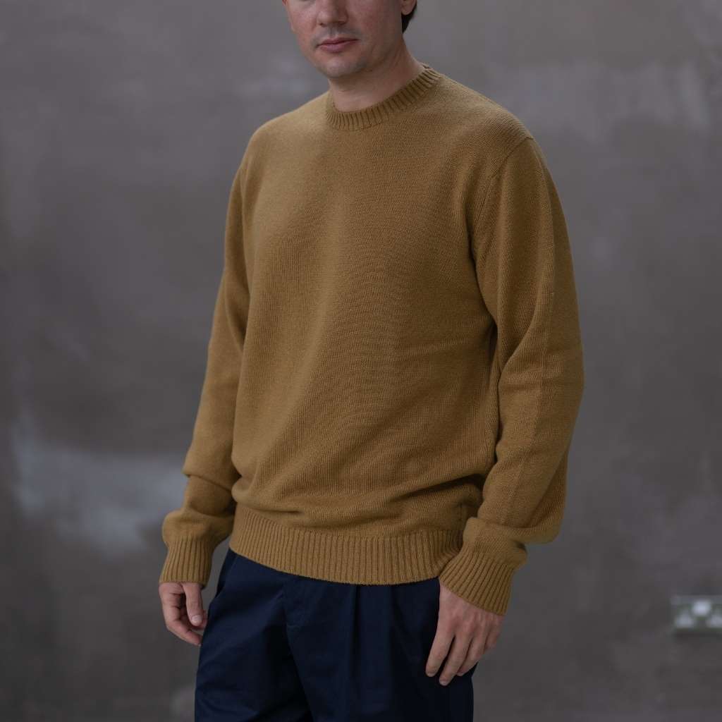 Man wearing a paradaiza mustard yellow sweater against a grey background