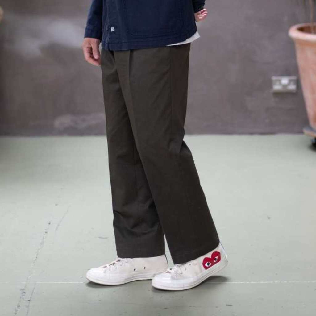 Person wearing paradaiza khaki chino pants and white sneakers with red accents on a plain floor.
