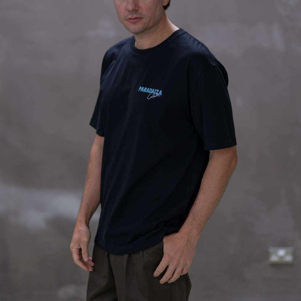 Man wearing a paradaiza black t-shirt with a logo on a gray background