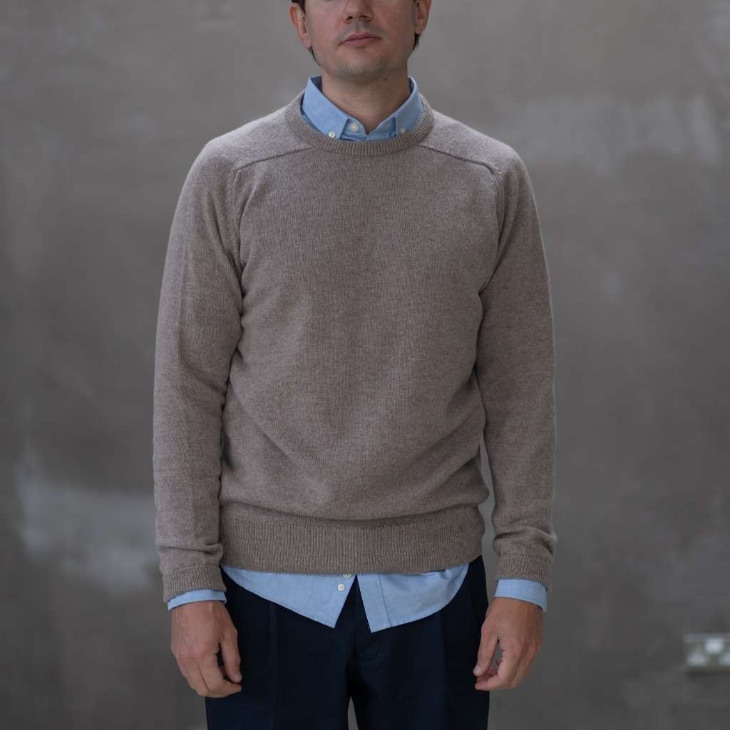 Man wearing a paradaiza brown sweater over a light blue shirt against a gray background