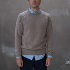 Man wearing a paradaiza brown sweater over a light blue shirt against a gray background