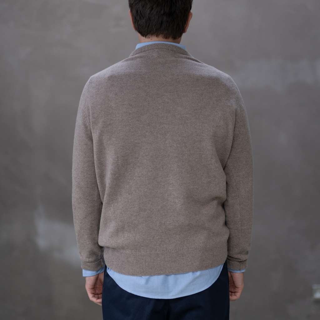 Man wearing a paradaiza brown sweater over a light blue shirt against a gray background