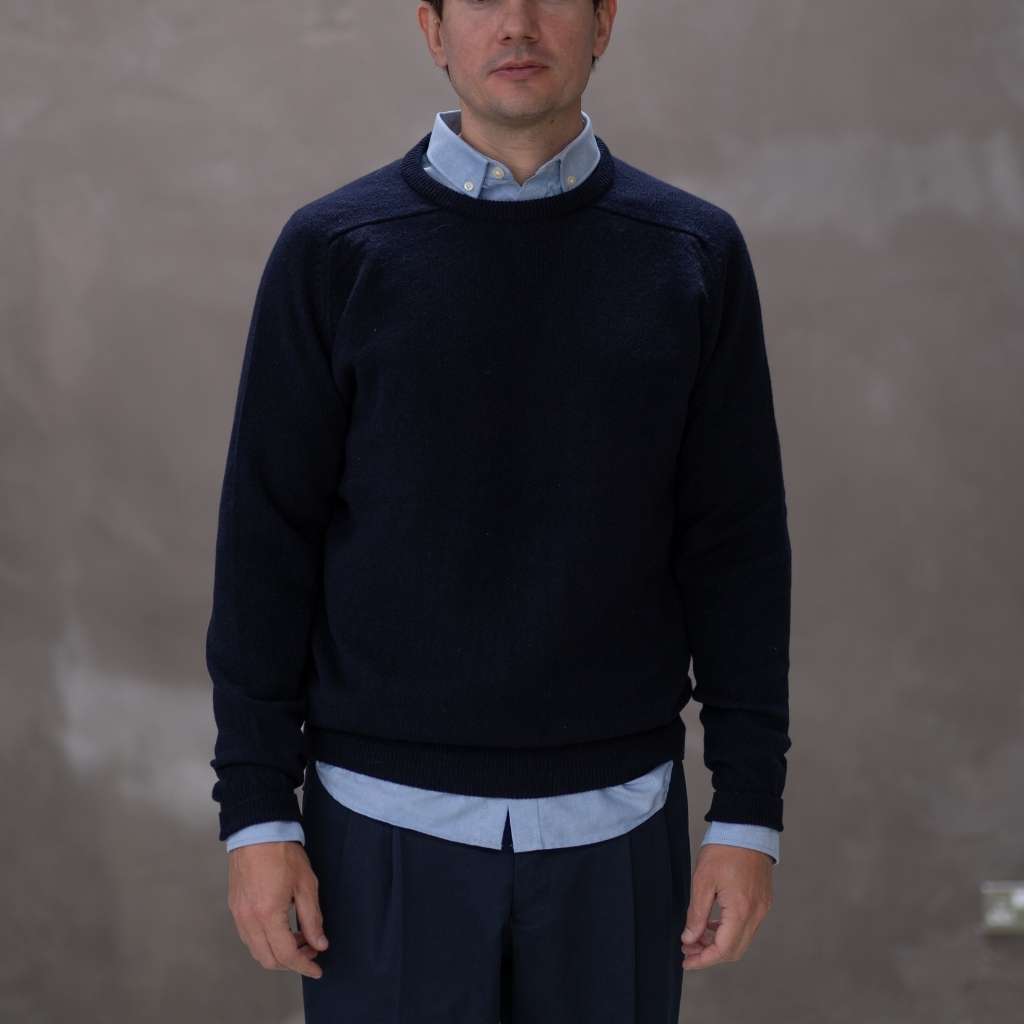 Man wearing a paradaiza navy sweater over a light blue shirt with a plain background