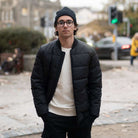 Man wearing a black paradaiza padded jacket and glasses standing on a street.