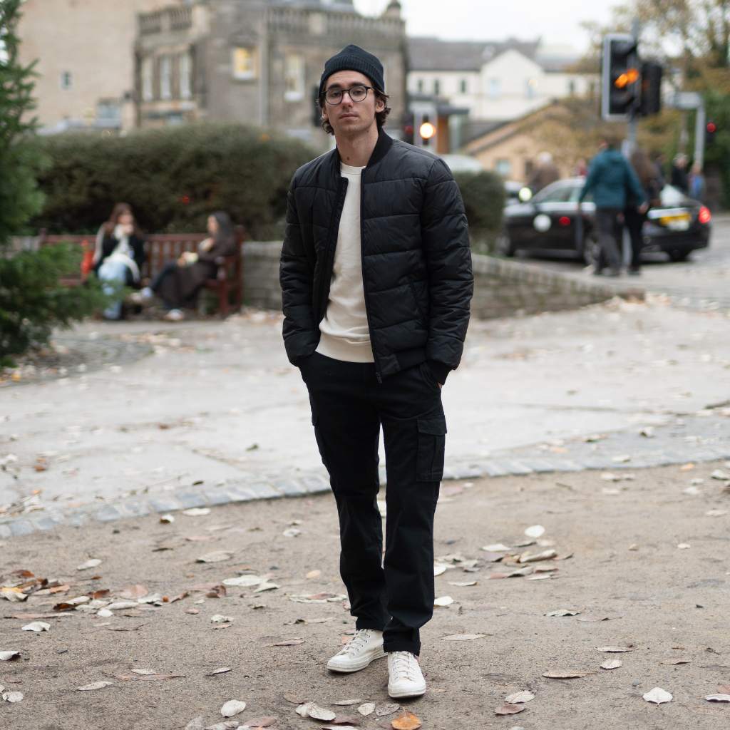 Man wearing a black paradaiza padded jacket and glasses standing on a street.