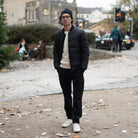 Man wearing a black paradaiza padded jacket and glasses standing on a street.
