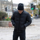 Man wearing a black paradaiza padded jacket and glasses standing on a street.