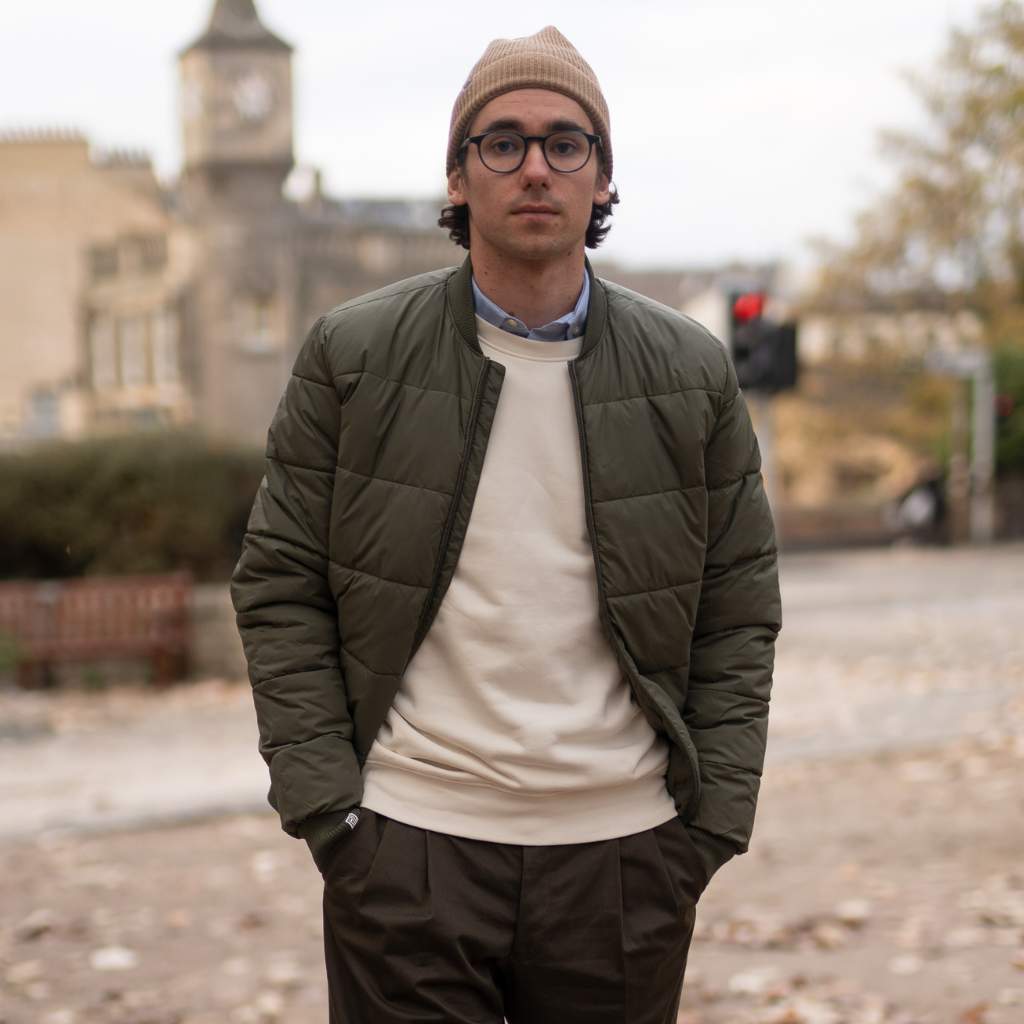 Man wearing a paradaiza khaki jacket and beige beanie standing outdoors with a blurred background