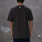 Person wearing a  paradiaiza black t-shirt with a  graphic on a gray background