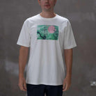 Person wearing a  paradaiza white t-shirt with a colorful graphic design on a gray background