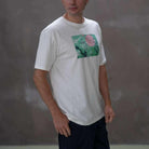 Person wearing a  paradaiza white t-shirt with a colorful graphic design on a gray background