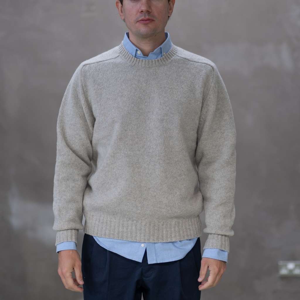 Man wearing a paradaiza beige sweater over a light blue shirt with a plain background