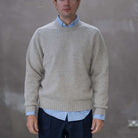 Man wearing a paradaiza beige sweater over a light blue shirt with a plain background