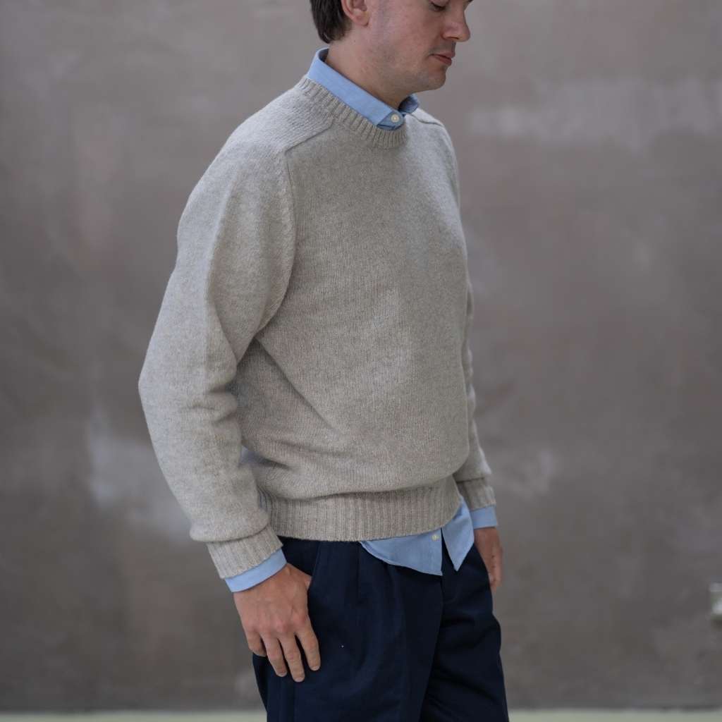 Man wearing a paradaiza beige sweater over a light blue shirt with a plain background