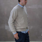 Man wearing a paradaiza beige sweater over a light blue shirt with a plain background