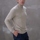Man wearing a paradaiza beige turtleneck sweater against a gray 
