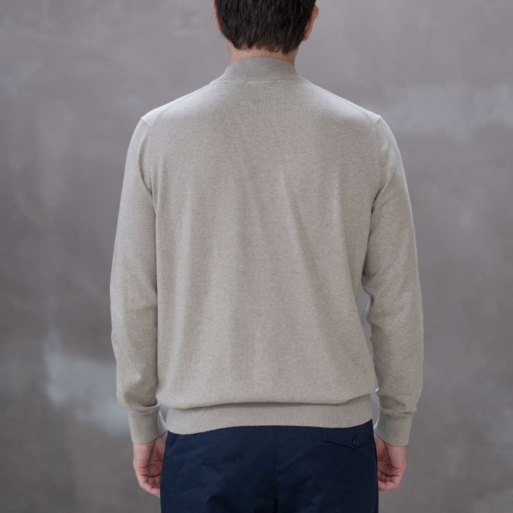 Man wearing a paradaiza beige turtleneck sweater against a gray 