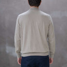 Man wearing a paradaiza beige turtleneck sweater against a gray 