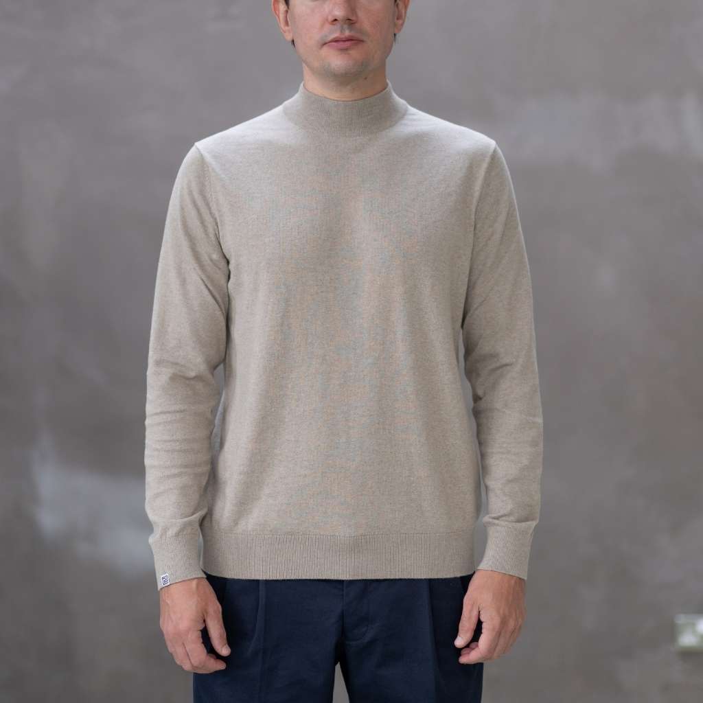 Man wearing a paradaiza beige turtleneck sweater against a gray background