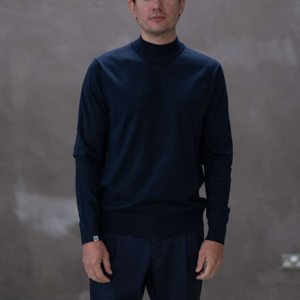 Man wearing a paradaiza  dark blue turtleneck sweater against a gray background