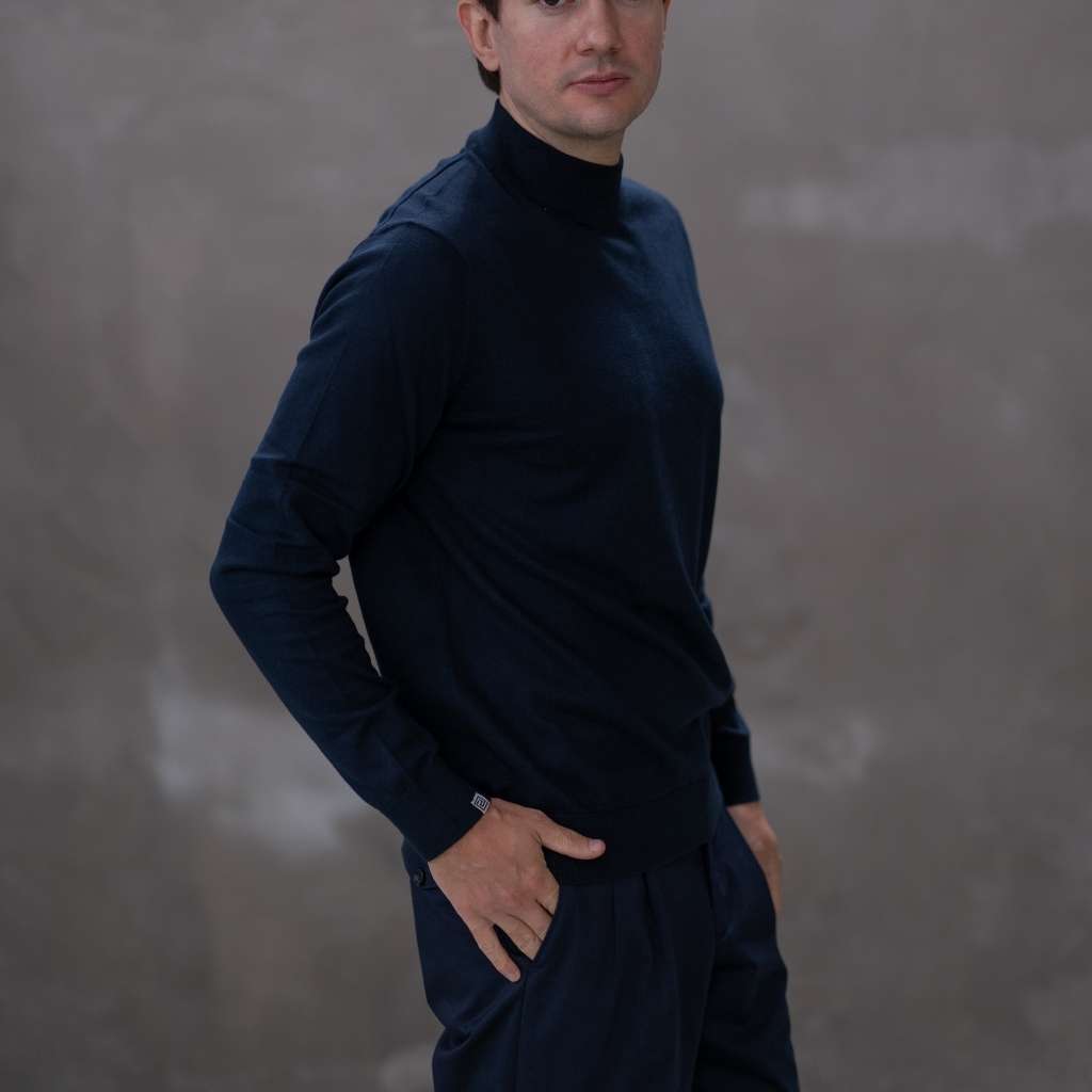 Man wearing a paradaiza  dark blue turtleneck sweater against a gray background