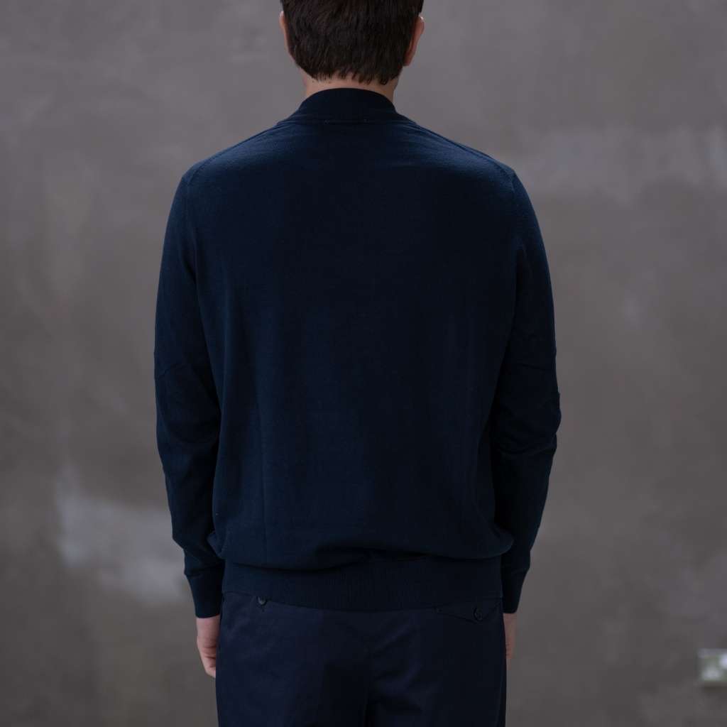 Man wearing a paradaiza  dark blue turtleneck sweater against a gray background