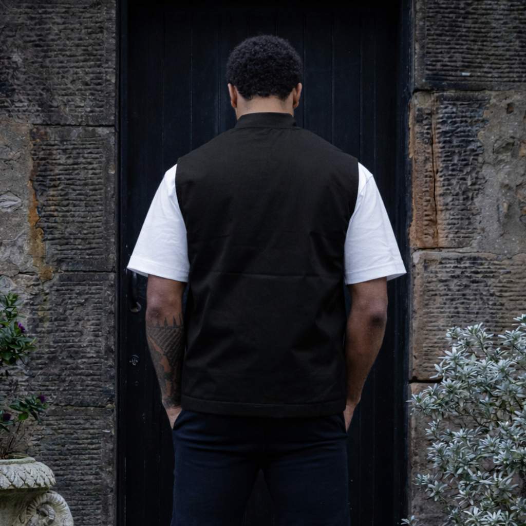 Man wearing a paradaiza black vest over a white shirt standing in front of a stone wall.