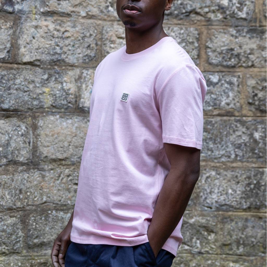 Person wearing a paradaiza pink t-shirt with a small logo against a stone wall.