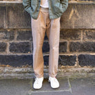 Person wearing paradaiza pinch chinos in  beige and white sneakers with a red heart design against a brick wall.