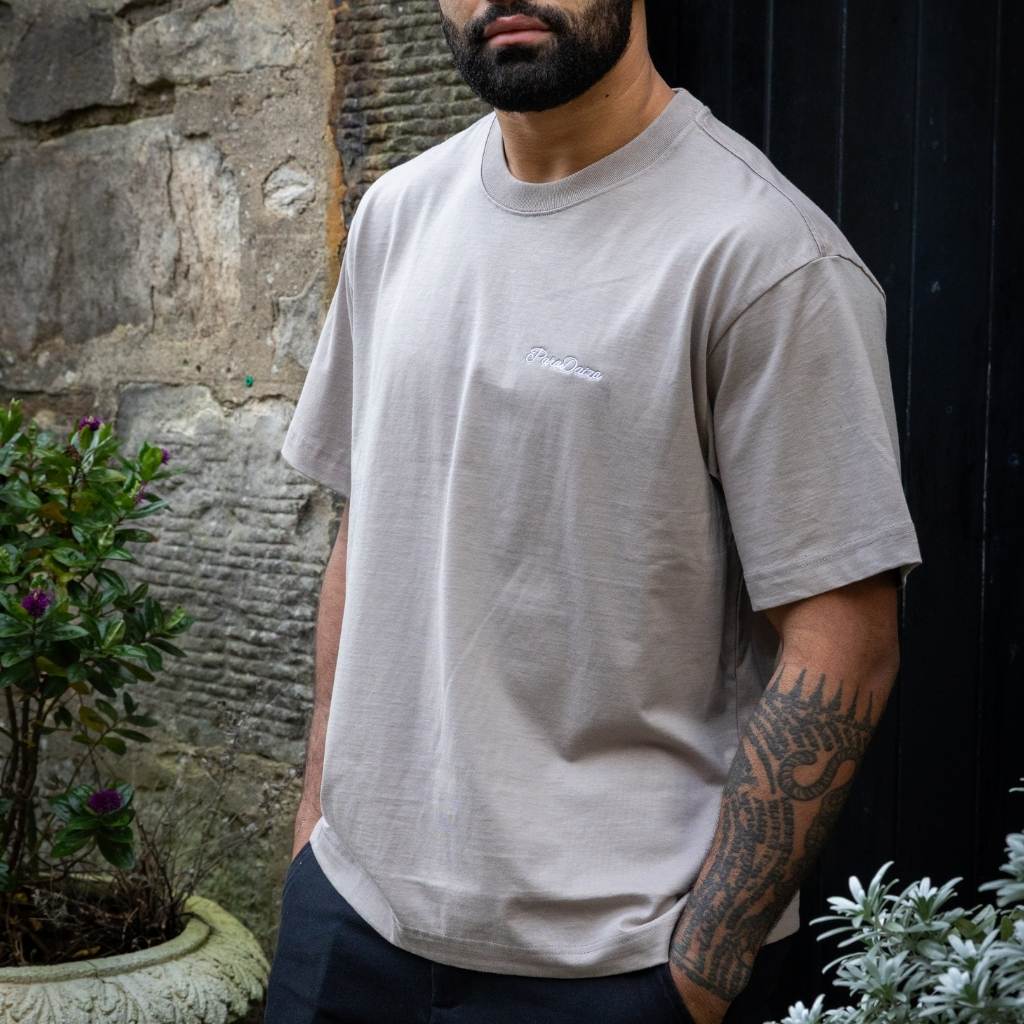 Man wearing a paradaiza t-shirt with a logo, standing outdoors against a stone wall.