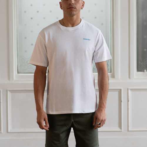 Man wearing a white t-shirt with a  paradaiza logo in a room with white walls 